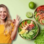 Ragazza che fa occhiolino e ok con la mano, di fianco a lei bow con insalate, sul tavolo insalata, lime e avocado