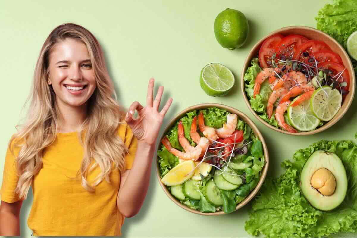 Ragazza che fa occhiolino e ok con la mano, di fianco a lei bow con insalate, sul tavolo insalata, lime e avocado